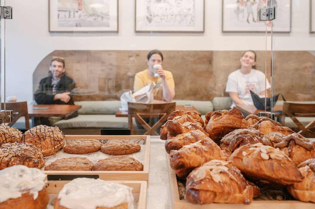 bakery display case filled with fresh pastries cookies and cinnamon rolls with customers seated in the background