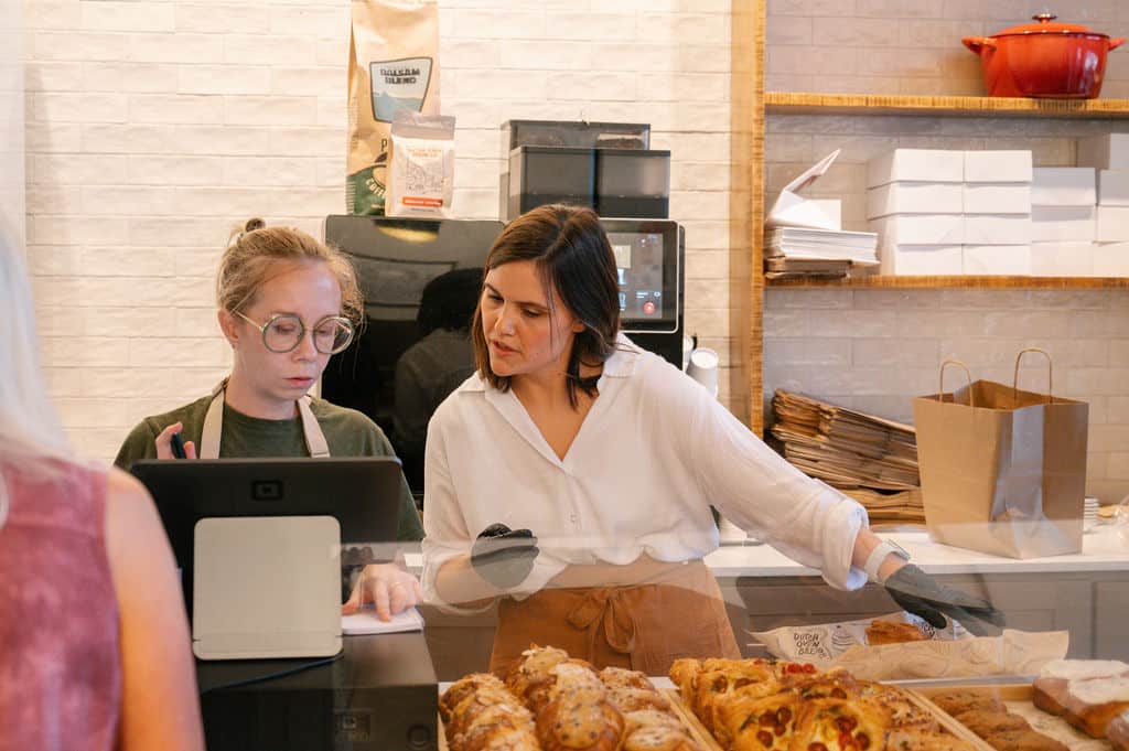bakery employee assisting customer at checkout with various pastries displayed