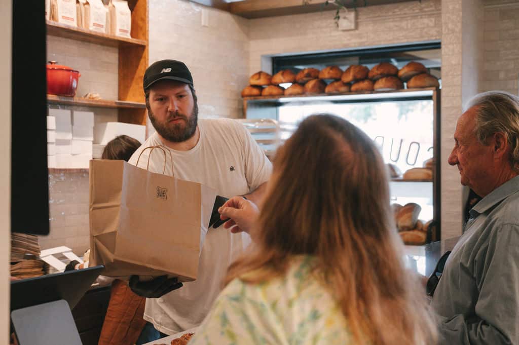 barista handing a paper bag to a customer in a cozy bakery