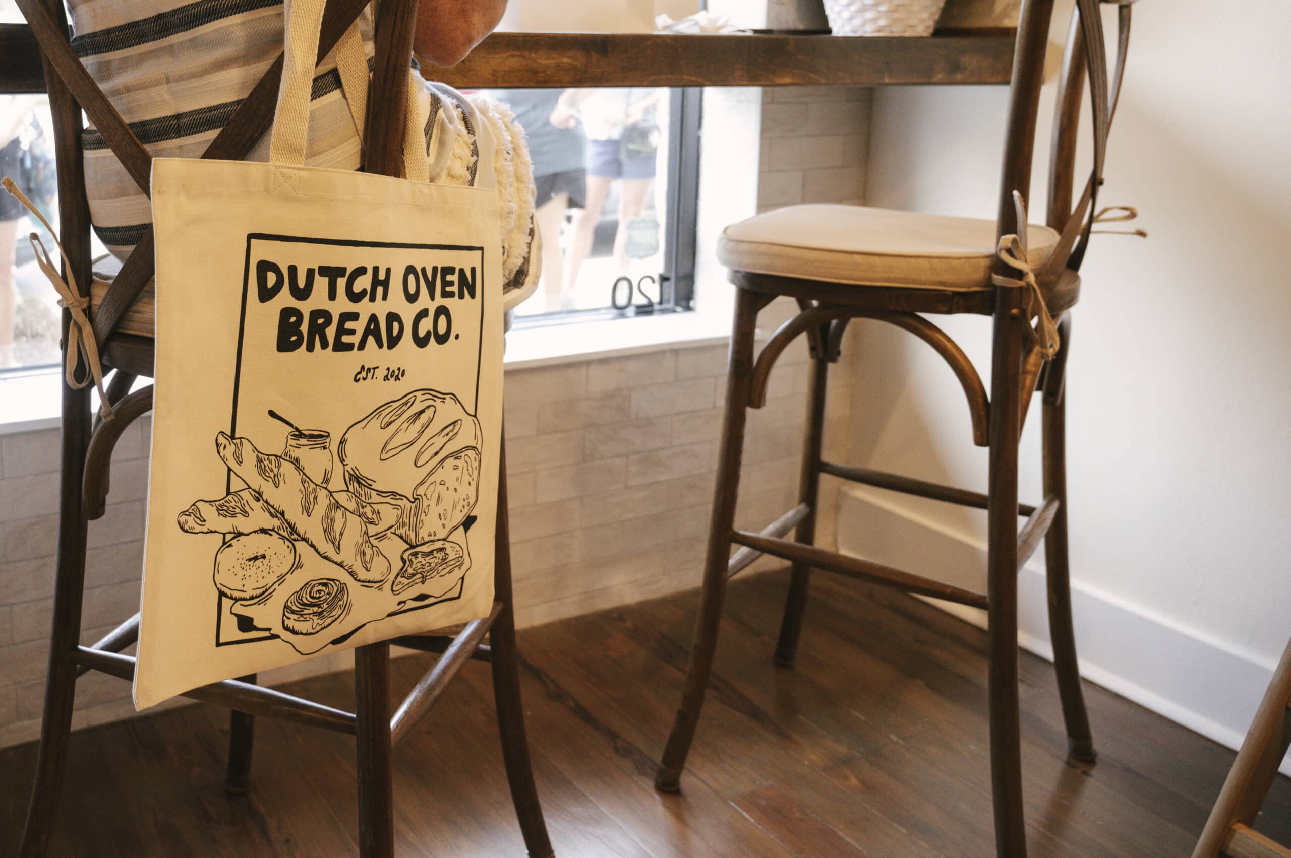 Dutch Oven Bread Co. tote bag hanging on a chair. Breads and pastries graphic. Est. 2020. New Smyrna Beach bakery.